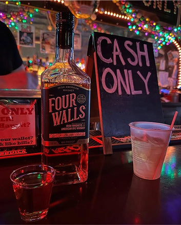 Bottle of Four Walls whiskey on a bar with a 'Cash Only' sign in the background.